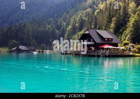 Restaurant und ein altes Holzboothaus am Ufer des Weissensees in der Sommerlandschaft der Alpen Berge, Österreich Stockfoto