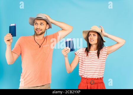 Verwirrt Mann und Frau berühren Hüte und halten Pässe auf Blau Stockfoto