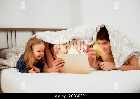 kaukasische Familie, Mutter Vater und Kinder liegen unter Decke auf dem Bett Video auf Tablet, Freizeit zu Hause. Stockfoto