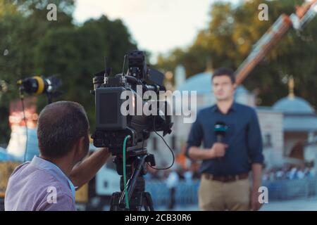 Hinter dem Szenenkonzept. Kameramann arbeitet an professionellen Kamera, die TV-Interviewer, professionelle Nachrichtenreporter macht Nachrichten im Freien. Stockfoto