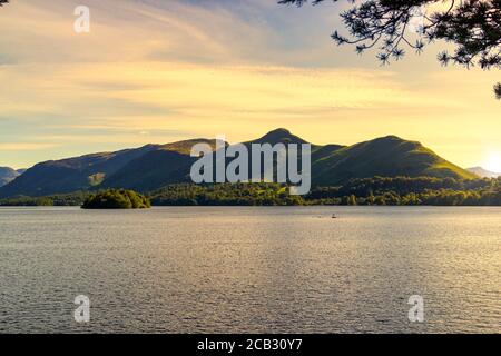 Sonnenbeschienene Derwentwater Seenoberfläche mit einer grünen Bergkette dahinter Durch Baumzweige gesehen Stockfoto