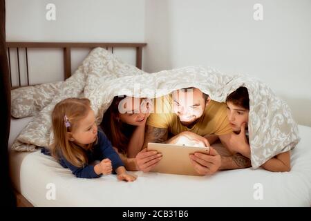 Freundliche Familie verbringen Zeit zusammen zu Hause mit Kindern, liegen auf dem Bett unter Bettdecke, in lässiger Kleidung Stockfoto