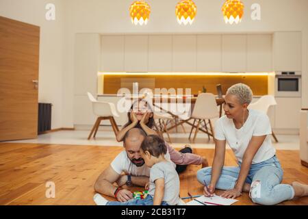 Familie Spaß zusammen im Wohnzimmer des Hauses. Mama, Papa und zwei Kinder auf dem Boden Zeichnung, lachen, spielen. Happy Family Konzept Stockfoto