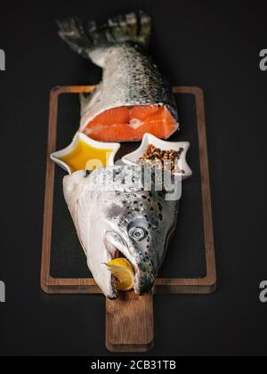 Frischer Lachs. Fischkopf und Schwanz auf einem Schneidebrett auf dunklem Hintergrund. Rote Fischsuppe mit Gewürzen, Zitrone und Olivenöl. Quelle von Nutzen OME Stockfoto