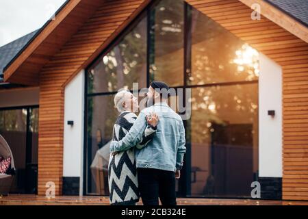 Rückansicht auf schönes Paar mit Blick auf neues Landhaus. Aufgeregt Mann und Frau, lächeln und glücklich zusammen Stockfoto