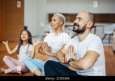 Junge kaukasische Eltern mit Kind meditieren zu Hause isoliert im Zimmer, sitzen auf dem Boden. Familie, Sport, Yoga-Konzept. Weiße Farben Stockfoto