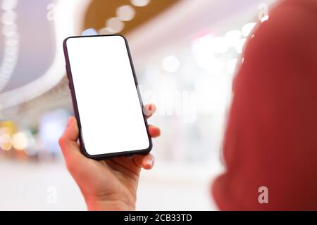 Eine Frau hält ein Telefon mit einem weißen Bildschirm in einem Einkaufszentrum. Stockfoto