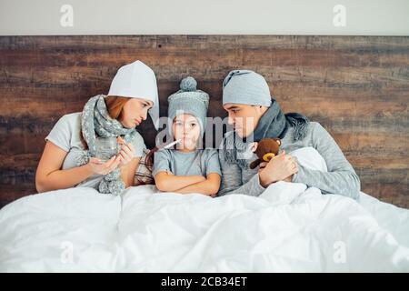 Portrait von kranken Mädchen Fieber, leiden an Schnupfen, Eltern liegen auf dem Bett zusammen mit ihr und unterstützen, Behandlung, tragen Hüte und Schals Stockfoto