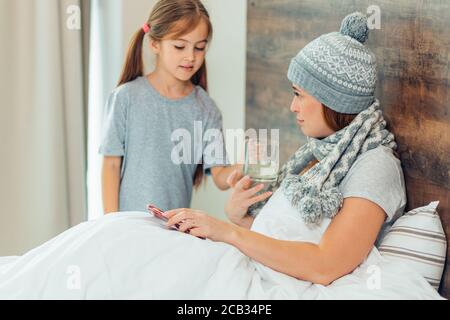 Ehrfürchtiges Kind kümmert sich um kranke, kranke Mutter, die an Krankheit leidet, Unterstützung für Kinder und die Aufmerksamkeit auf die Mutter, die auf dem Bett liegt Stockfoto
