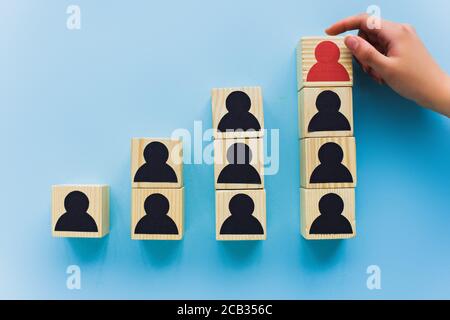 Teilansicht der Hand in der Nähe von Holzblöcken mit schwarzen und roten menschlichen Ikonen auf blauem Hintergrund, Führung und Karriere Leiter Konzept Stockfoto