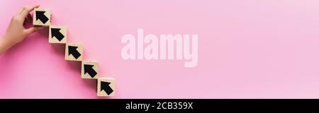 Teilansicht der Hand in der Nähe von Holzblöcken mit schwarzen Pfeilen auf rosa Hintergrund, Geschäftskonzept Stockfoto