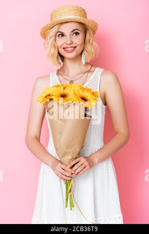 Junge Frau in Strohhut mit gelben Blüten auf rosa Stockfoto