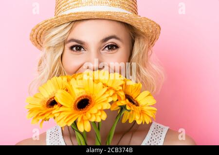 Junge Frau in Strohhut bedeckt Gesicht mit gelben Blumen Auf Rosa Stockfoto