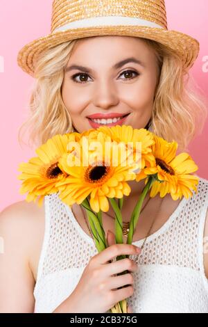 Junge Frau im Strohhut, die blühende gelbe Blumen auf hält Rosa Stockfoto