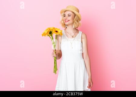 Frau in Strohhut und weißem Kleid mit gelben Blumen Auf Rosa Stockfoto