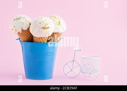 Eiszapfen in einem blauen Eimer und kleines weißes Fahrrad auf einem rosa Hintergrund. Eine Eiscreme im Waffelstil. Stockfoto