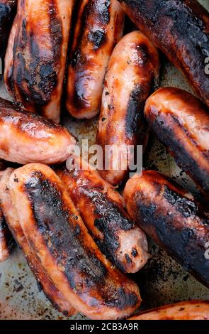 Brutzelnde Schweinswürste auf Metall-Grillplatte Stockfoto