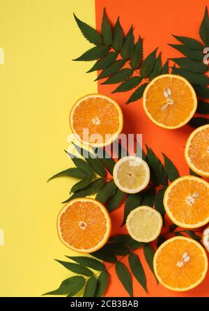 Komposition aus Hälften von Zitronen und Orangen mit grünen Blättern auf einem hellgelb-orangen Hintergrund, Flat Lay Stockfoto