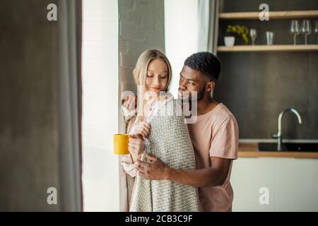 Schönen afrikanischen Kerl küsst seine kaukasischen Freundin am Hals von hinten, zu Hause in der Küche Zimmer mit modernem Interieur Stockfoto