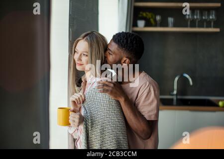 Multi-ethnischen Beziehungen Konzept. Afrikanische jungen Mann auf seine weiße Haut Frau mit liebevollen und fürsorglichen Ausdruck, die Sie mit einem warmen blan Stockfoto