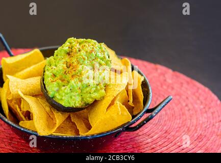 Nachos mit Avocado in schwarzer Metallschale, Guacamole Stockfoto