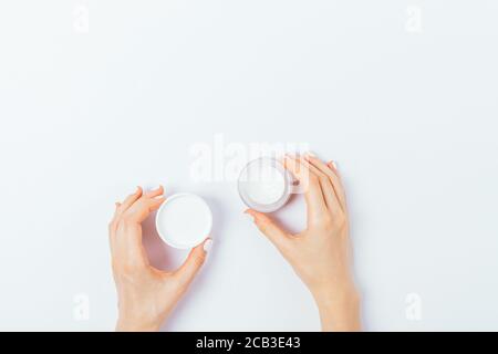 Draufsicht der weiblichen Hände mit offenem Glas und Deckel der kosmetischen Gesichtscreme auf weißem Tisch. Stockfoto