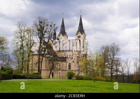 Kirche der Geburt der Jungfrau Maria, Orlova, Schlesien, Tschechische Republik / Tschechien - neugotisches Sakralgebäude in einem wunderschönen grünen Park während der Sprotte Stockfoto