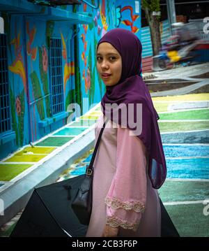 Kuala Lumpur/Malaysia/24 May 2020: Junge schöne muslimische Mädchen mit einem lila Kopftuch und einem rosa Kleid in Jalan Alor, Malaysia Stockfoto