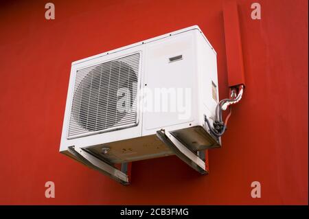 Klimaanlage - Elektronische Vorrichtung zum Kühlen von heißen und warmen Temperaturen. Weiße Klimaanlage ist an der roten Wand platziert Stockfoto