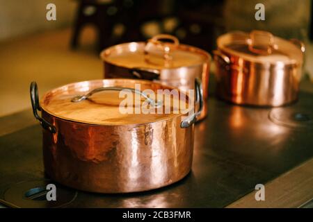 Nahaufnahme von Kupfertöpfen mit geschlossenen Deckeln auf einem antiken Brennerofen. Stockfoto