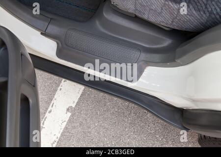 Nahaufnahme eines Auto-Trittbretts mit einer offenen Tür mit einer grauen Kunststoffverkleidung an der Schwelle eines weißen japanischen Crossover nach Pre-Sale-Vorbereitung. Stockfoto