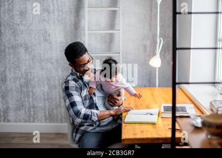 Junger afrikanischer Mann kümmert sich um sein kleines Kind während der Arbeit zu Hause. Nahaufnahme Foto Stockfoto