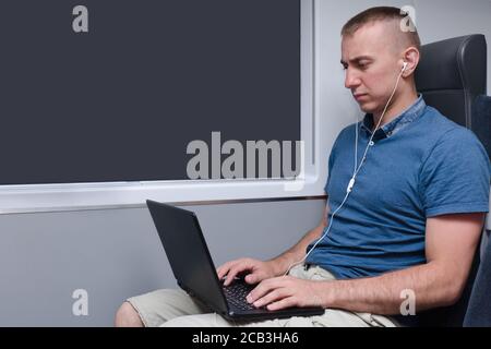Junger Mann, der hinter einem Laptop in einem Zug sitzt Stuhl Stockfoto