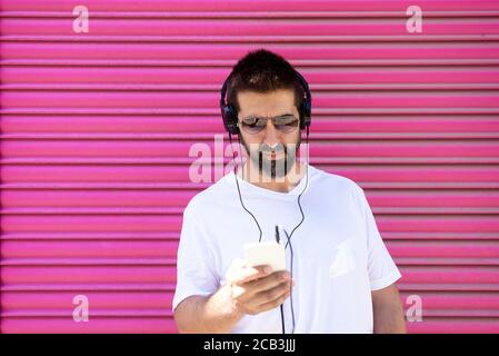 Bärtiger Kerl mit Kopfhörern und Sonnenbrillen mit einem Smartphone während Musik hören Stockfoto