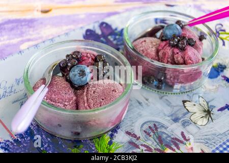 Köstliches hausgemachtes Lavendeleis in einer Glastasse mit Heidelbeeren und Waldbeeren, aus nächster Nähe Stockfoto