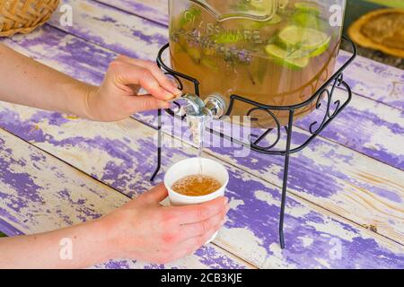 Hausgemachte Limonade in Vintage-Glas mit Lavendel, Zitronen und Limetten Scheiben auf einem Holztisch, Mädchen füllt ein Glas mit Händen Stockfoto