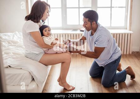 Schöner Afro Kerl setzen auf Socken auf seinem Baby die Füße, Kinderbetreuung. In voller Länge Seitenansicht Foto Stockfoto