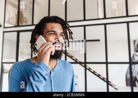 Fröhlicher junger afrikanischer Mann mit Handy, während er im Stehen Die Wohnung Stockfoto