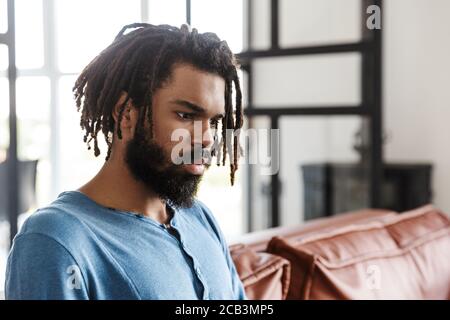 Hübscher junger afrikanischer Mann, der zu Hause auf einer Ledercouch sitzt und wegschaut Stockfoto