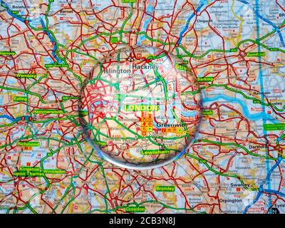 Nahaufnahme eines Kuppellupenglases über einer Straßenatlas-Karte des Großraums London, mit London selbst in der Mitte, vergrößert für eine genauere Ansicht. Stockfoto