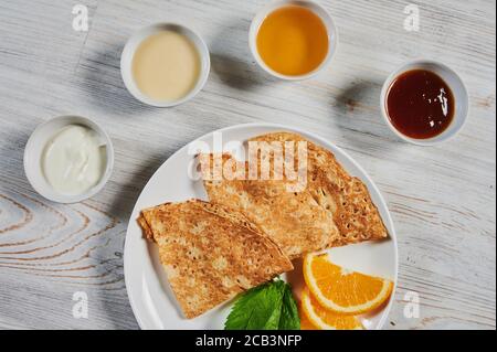 Crepes mit saurer Sahne auf weißem Teller, Kopierer Platz. Leckere hausgemachte Crepes zum Frühstück.Dünne drei Crepes oder Pfannkuchen mit Butter, Honig und sauer Stockfoto