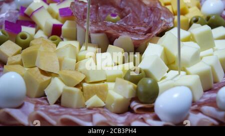 Weißes Gericht mit Salami, Schinken, Wachteleiern und grünen Oliven, auf einem Hintergrund mit einer blau-weißen Tischdecke, im Foto-Zoom mit Details Stockfoto