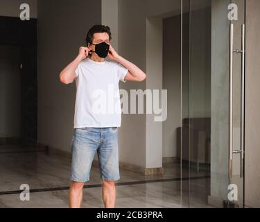 Ein Mann in weißem T-Shirt trägt eine schwarze Gesichtsmaske, wenn er das Haus verlässt, um sich vor Staub, Smog, Stockfoto