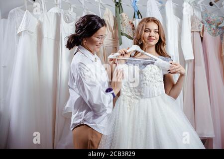 Schöne kaukasische Frau versuchen, zukünftige Hochzeitskleid von Designer in ihrem eigenen Salon gemacht, Blick auf Kleid mit Liebe, Traum Stockfoto