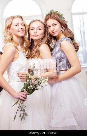 Drei kaukasische Freundinnen versuchen auf Hochzeitskleider im Salon, schöne Frauen zusammen in weißen Kleidern im Salon Stockfoto