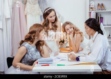 Gut aussehende Erwachsene Frau Schneider, Designer von Hochzeitskleider beraten junge Frauen Bräute, nehmen ihre Maßnahmen, um geeignete Größe und Stil zu machen Stockfoto