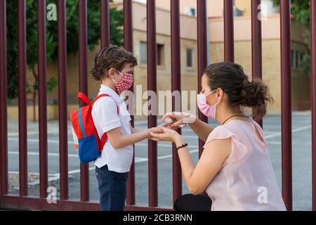 Eine Frau, die einem Schuljungen an der Tür einer Schule alkoholisches Gel auf die Hände legt. Konzept der neuen Normalität in der Schule während der Covid19 p Stockfoto