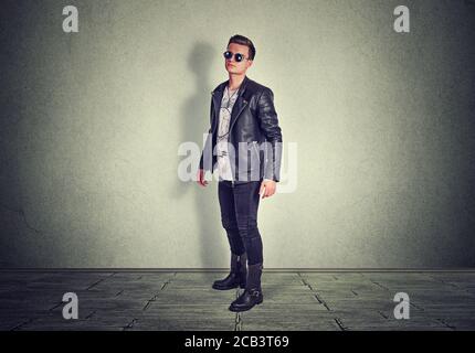 Portrait von selbstbewussten jungen Mann auf Sie Kamera stehend im Studio isoliert auf grauen Wand Hintergrund. Horizontales Schussmodell in schwarzem Leder Jack Stockfoto