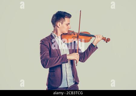 Musikleidenschaft, Hobby-Konzept. Der junge Mann, der modern und elegant gekleidet ist, spielt auf einer Holzvioline in einem Studio, das auf einem hellgrünen Wandhintergrund isoliert ist. H Stockfoto