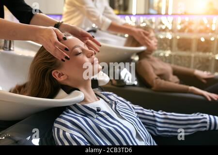 Junge und schöne kaukasische Mädchen liegen auf einem speziellen Sofa, während professionelle Friseure waschen ihre Haare für die Farbänderung, Färben im Schönheitssalon Stockfoto